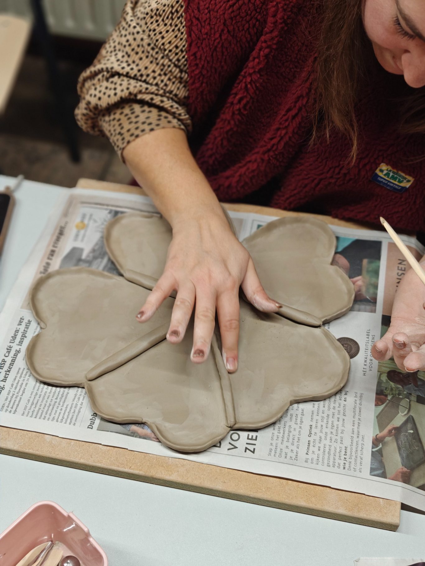 Vrouw vormt een kleiobject in de vorm van een bloem op een werktafel.