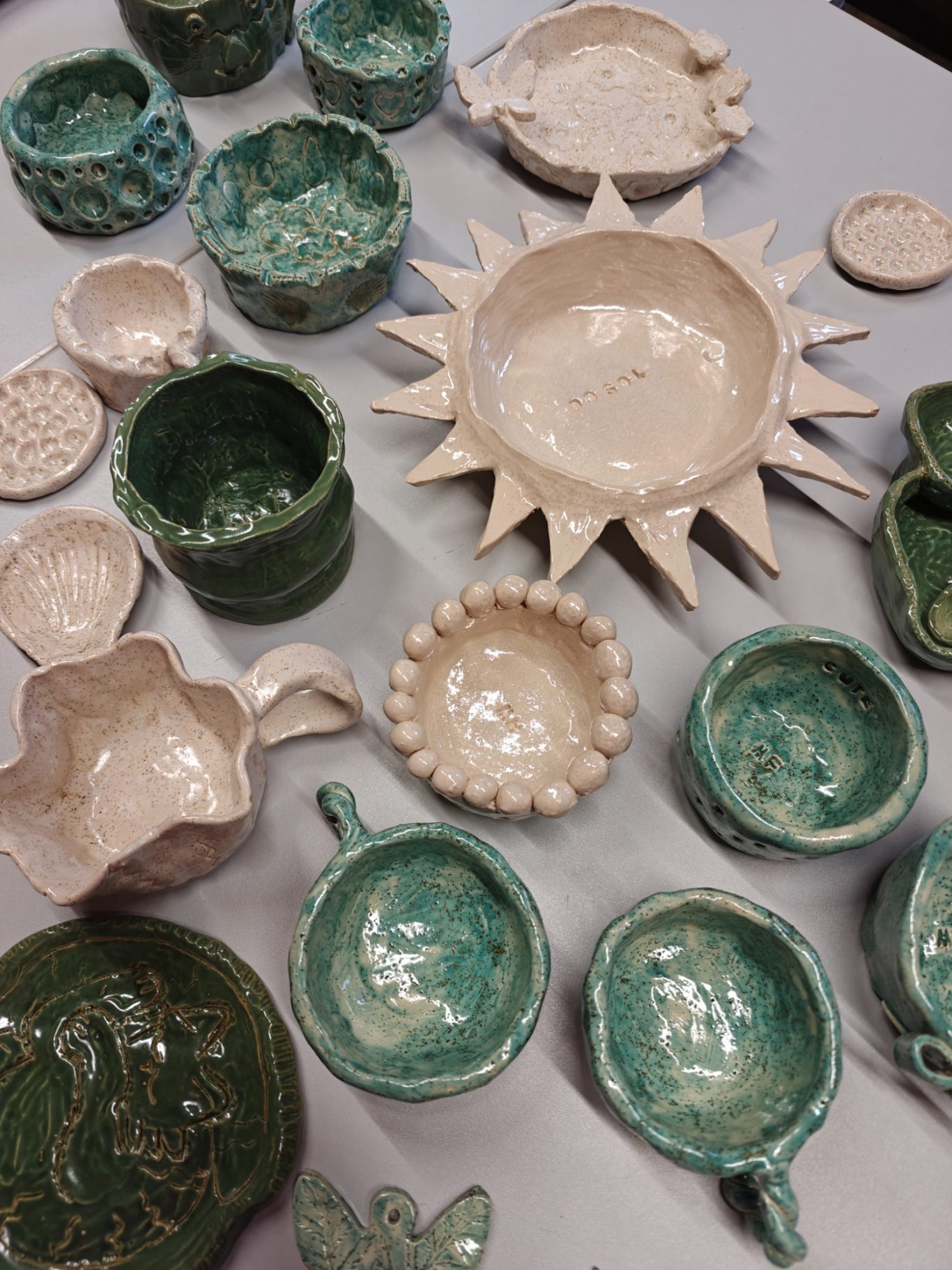 Divers keramiekwerk met verschillende vormen en glazuren in groene en witte tinten.