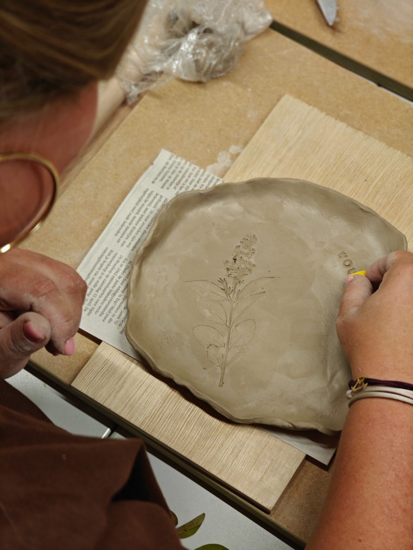 Een persoon sculpt een ronde kleiplaat op een houten werkblad.