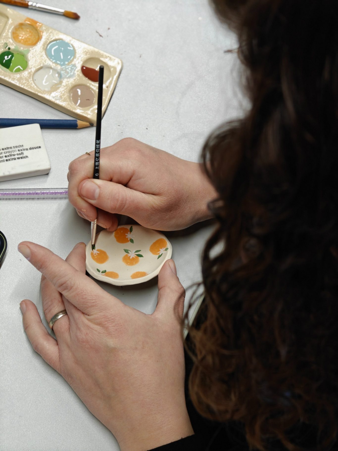 Een hand schildert met glazuur een theeschaaltje met sinaasappels.