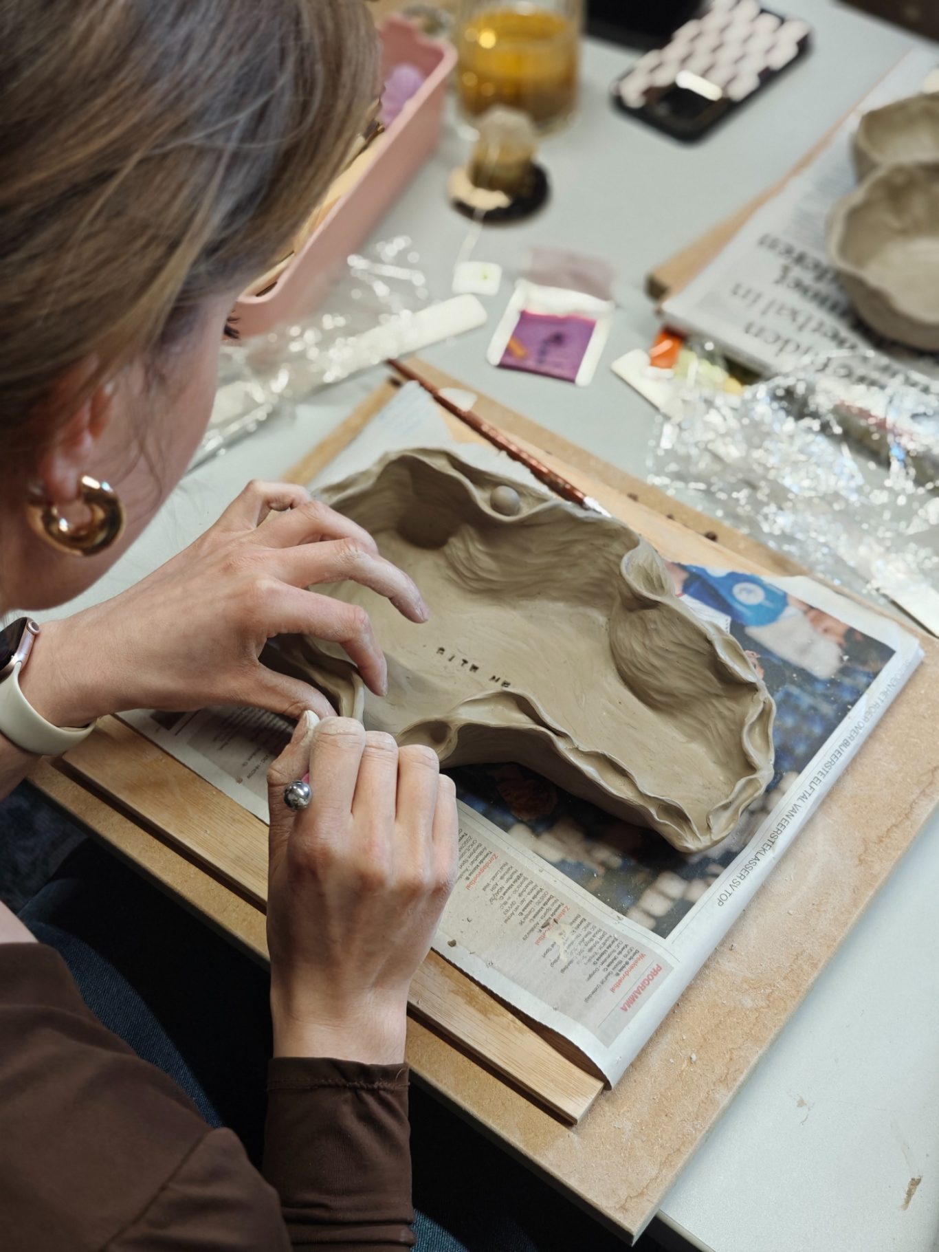 Een persoon werkt met klei en maakt een schotel op een werktafel.