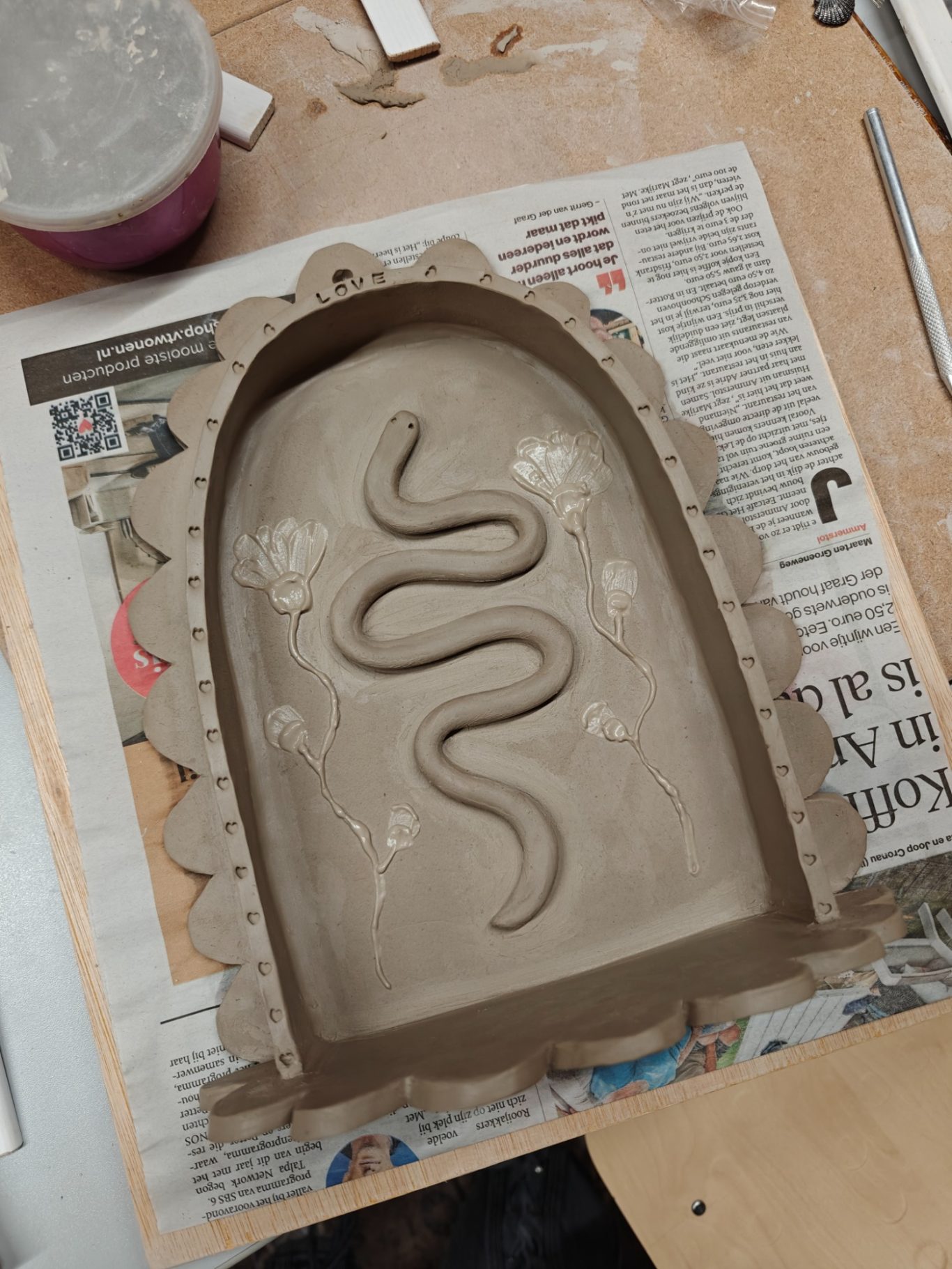 Klei vorm met een slangmotief en versieringen, op een werkblad.