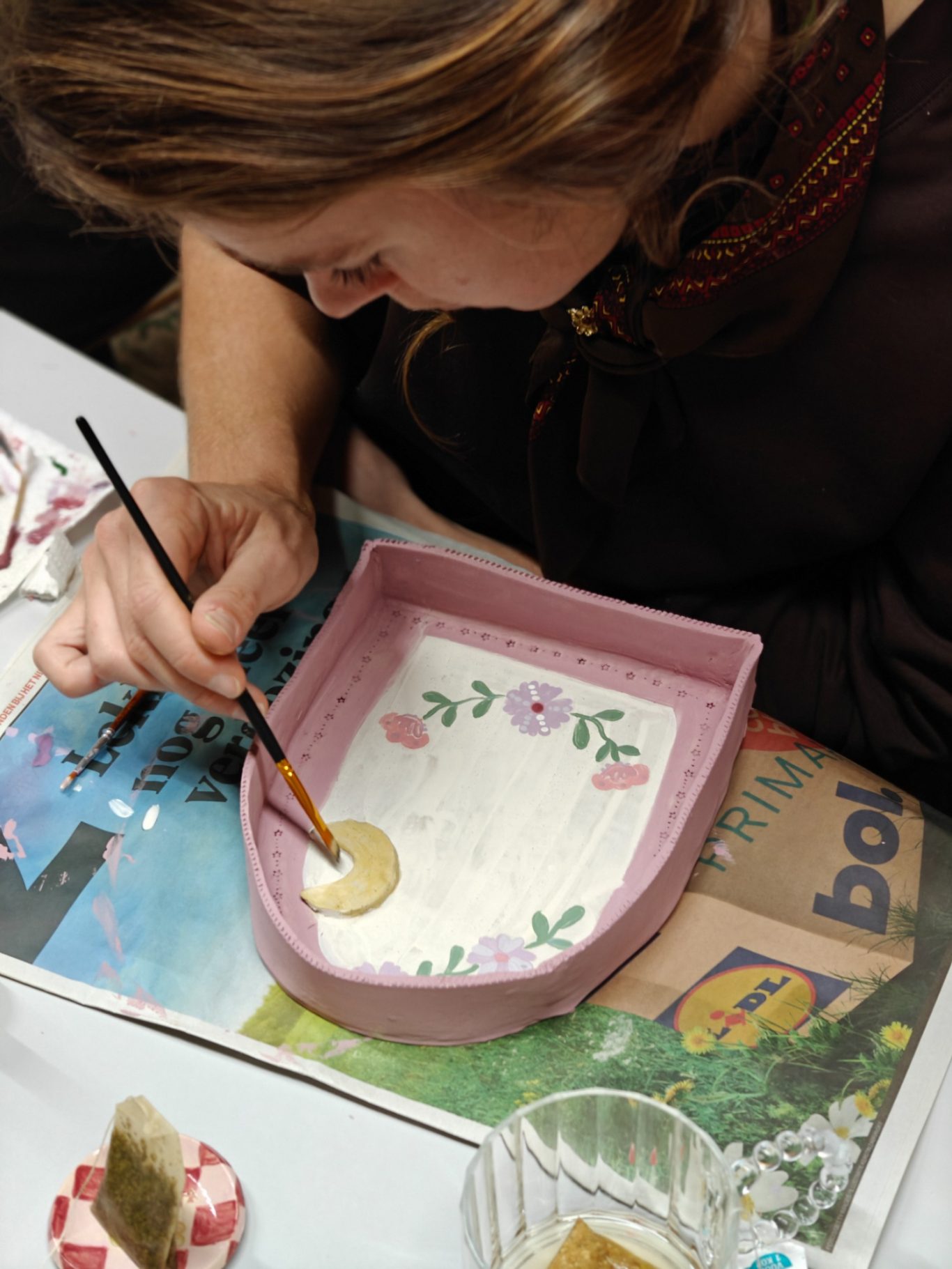 Vrouw schildert bloemen op een roze schaal met een penseel.